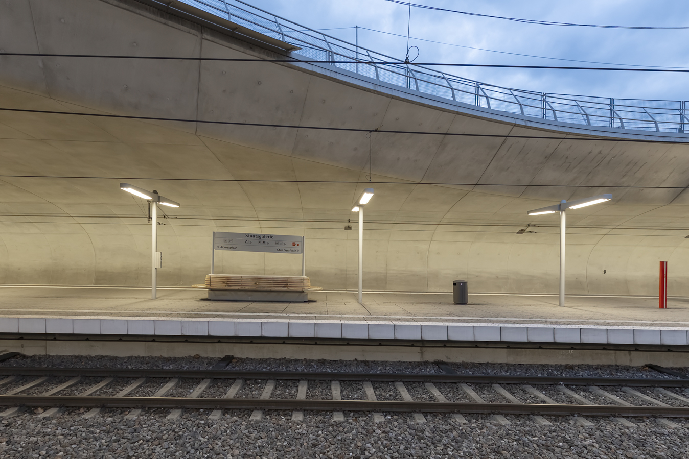 Arrêt de tramway Staatsgalerie à Stuttgart, vue sur le quai spacieux et moderne avec un éclairage LED uniforme et un mur en béton voûté en arrière-plan.