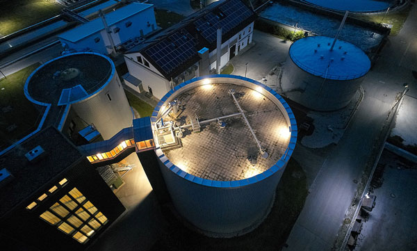 Industrial lighting at the Neufinsing wastewater treatment plant with BASEL LED, LUZERN 38 LED, ZUG LED, and URANUS highlights technical equipment, tanks, and basins from an aerial perspective.