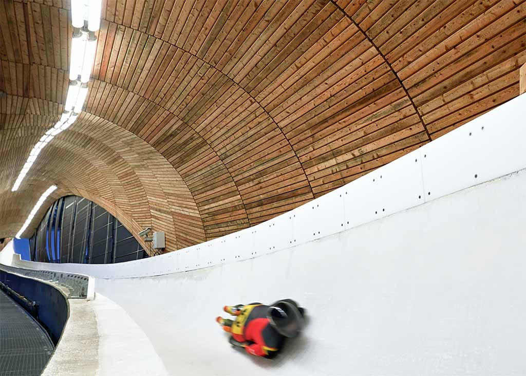 A skeleton racer hurtles through an ice track with NORKA luminaires mounted on the ceiling